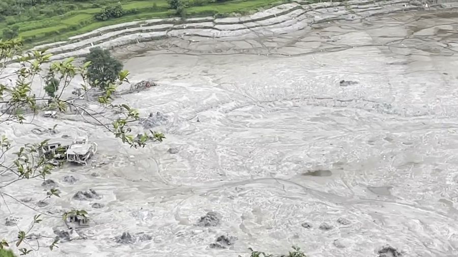 A video across a valley floor buried in gray mud and braided channels of water, with two broken concrete buildings at the edge.