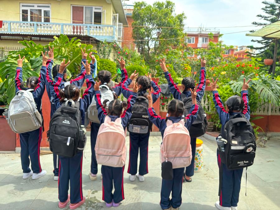 Children with backpacks waving as they leave the orphan home for school